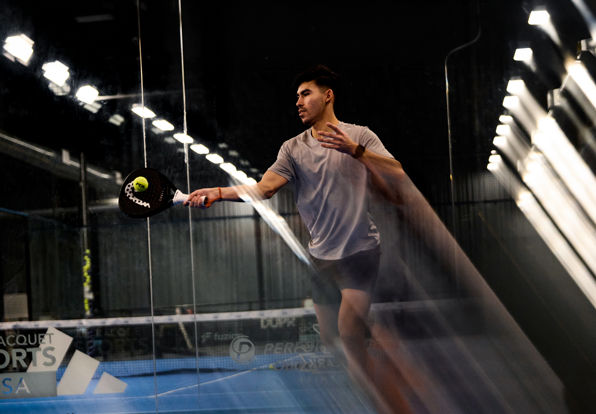 Person playing indoor tennis with a racket and ball in a well-lit indoor court.